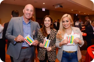 2 women and a man holding up colorful stickers smiling